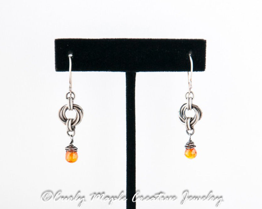 Silver Chainmaille Orange Teardrop Earrings hanging from a jewelry stand